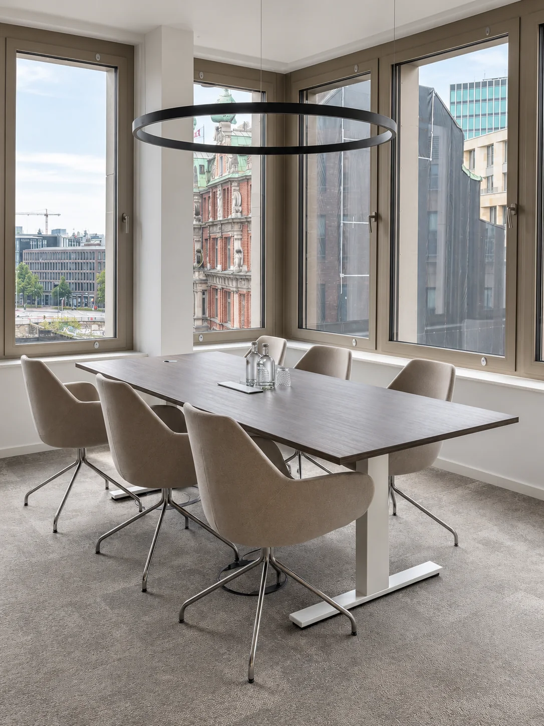 Heller Besprechungsraum mit einzelnem Konferenztisch, beigefarbenen Stühlen und schwarzer Ringlampe, Blick auf die Hamburger Innenstadt